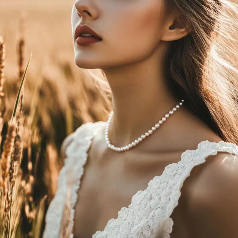 Close-up of a female model's neck and cheek wearing a pearl necklace and a white dress, with an autumn rice field in the background.