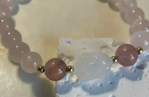 8mm pink rose quartz beaded bracelet with a clear rabbit crystal on a white base.
