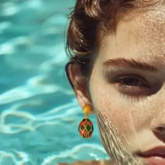 Female model wearing colorful drop earrings in a swimming pool.