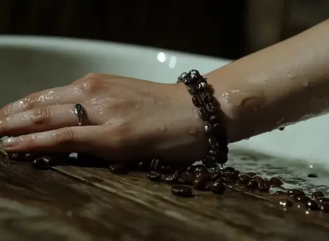 Close-up of female model's wrist wearing a coffee bean and alloy bracelet, with a bathtub in the background