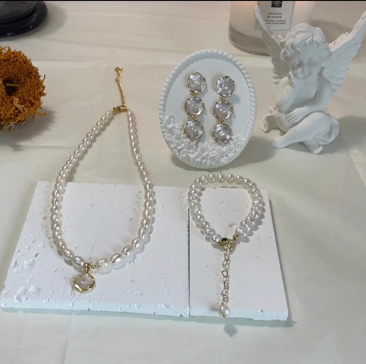 Freshwater Pearl Jewelry Set featuring a bracelet, earrings, and necklace on a white base with a dry sunflower and plaster angel in the background.