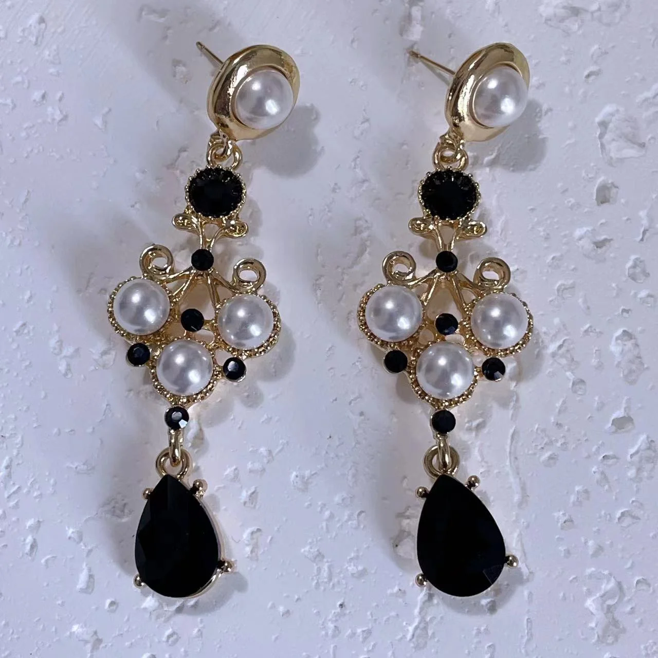 Vintage black & white 14K gold-plated long drop earrings on white plaster board.
