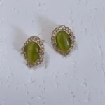 Vintage olive green cat’s eye glass stud earrings on a white plaster board.