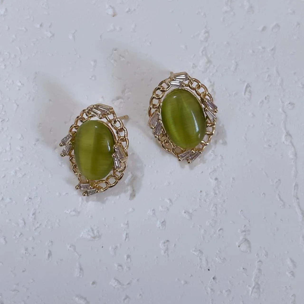 Vintage olive green cat’s eye glass stud earrings on a white plaster board.