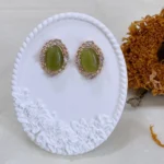 Vintage olive green cat’s eye glass stud earrings on a white plaster stand with a dried sunflower behind.