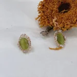 Vintage olive green cat’s eye glass stud earrings placed on white fabric with a dried sunflower in the background.