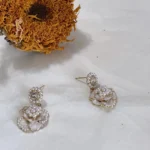 Vintage camellia pearl drop earrings with enamel and rhinestones placed on white fabric with a dried sunflower behind.