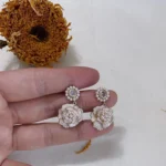 Model showcasing vintage camellia pearl drop earrings with enamel and rhinestones, holding a dried sunflower.