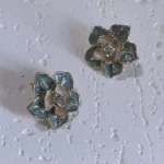 Vintage blue enamel camellia 14K gold-plated stud earrings on white plaster board.