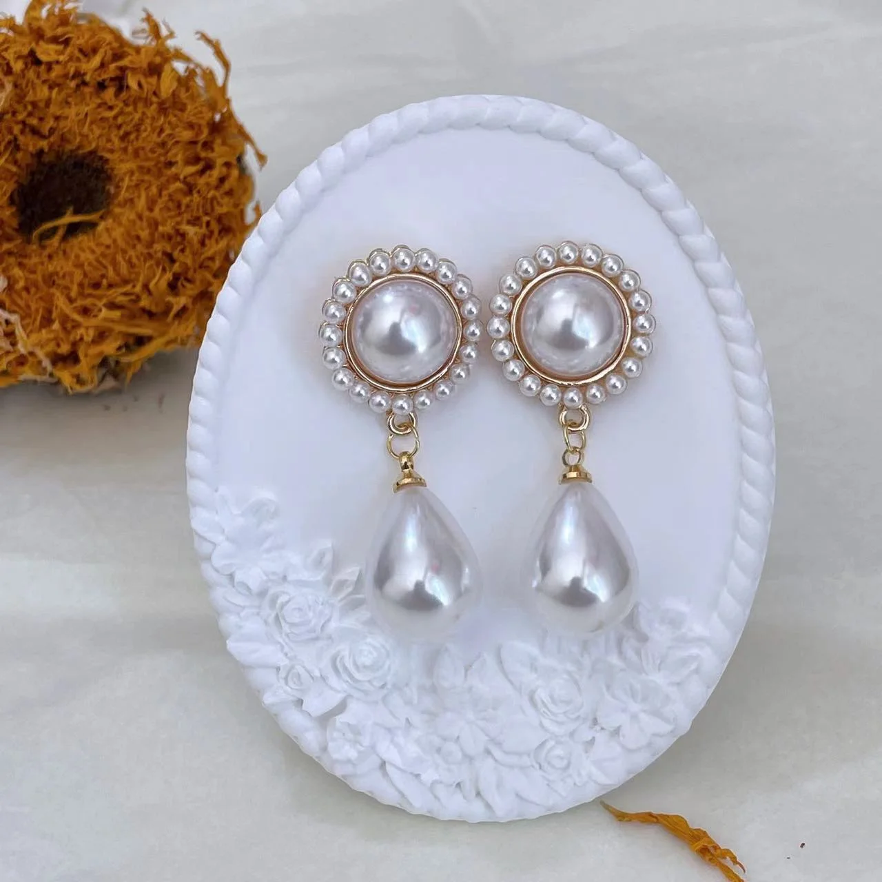 Vintage baroque pearl floral 14K gold-plated drop earrings displayed on a white plaster stand with a dried sunflower in the background.