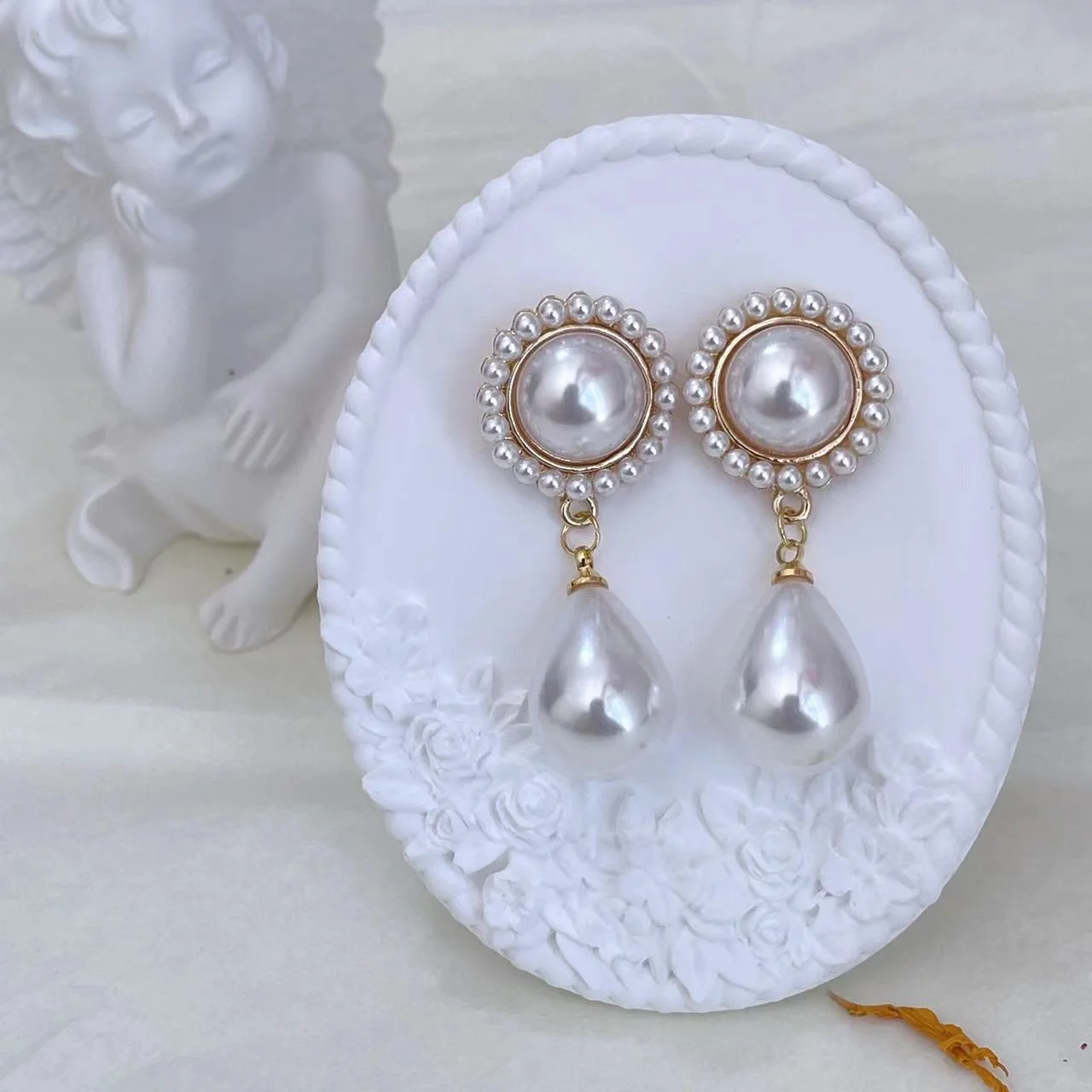 Vintage baroque pearl floral 14K gold-plated drop earrings on white plaster stand with an angel statue in the background.
