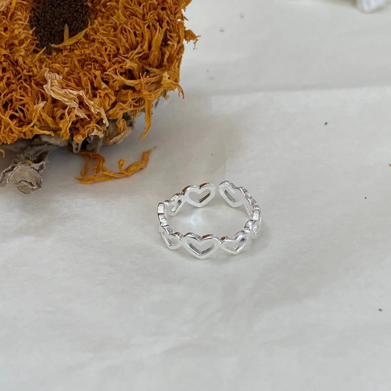 Silver-Plated Hollow Heart Open Ring on fabric with dried sunflower