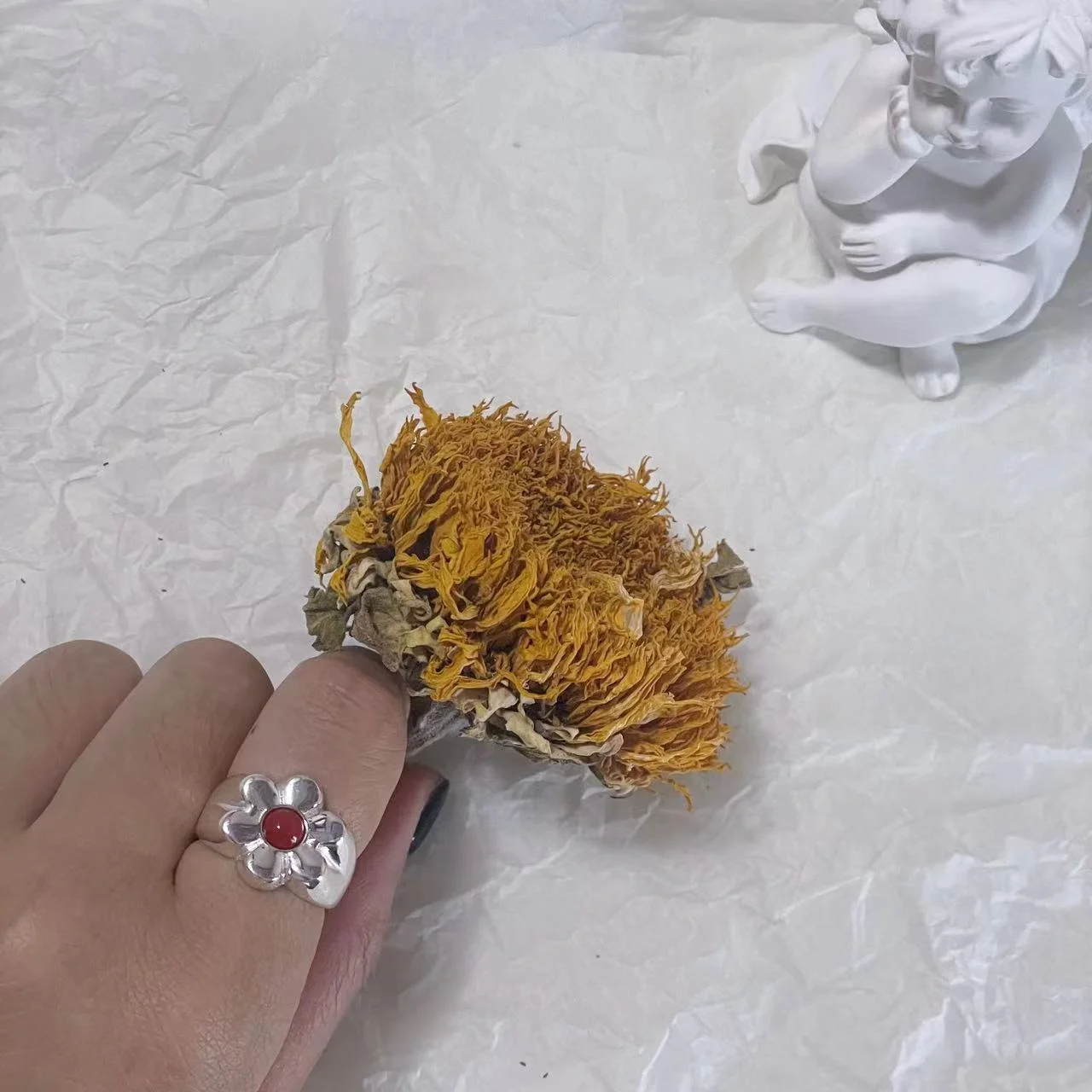 925 Sterling Silver Floral Ring with Red Natural Stone, Model Holding a Dried Sunflower with Angel Figurine in the Background